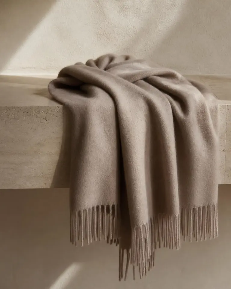 A warm taupe fringed cashmere scarf draped over a travertine ledge.