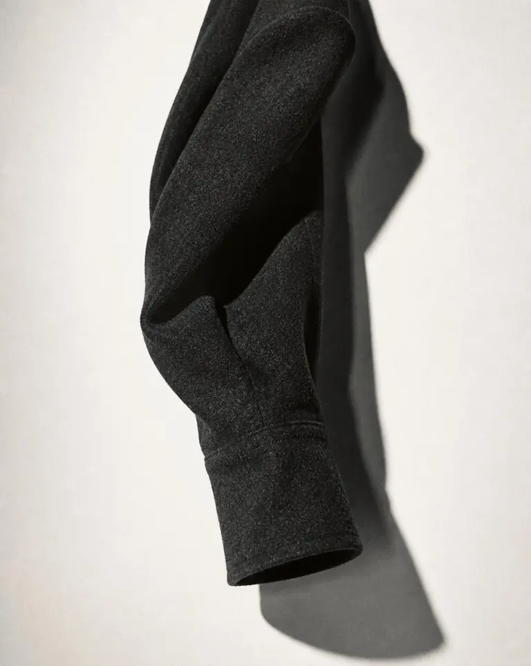 A charcoal wool sleeve suspended against a bone backdrop.